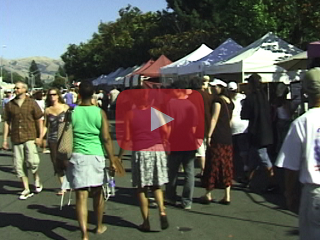 Play button showing crowd walking past festival booths