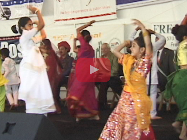 Play button showing female Indian dancers on stage with men seated in the background.