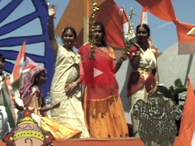 Play button showing Indian women on parade float.